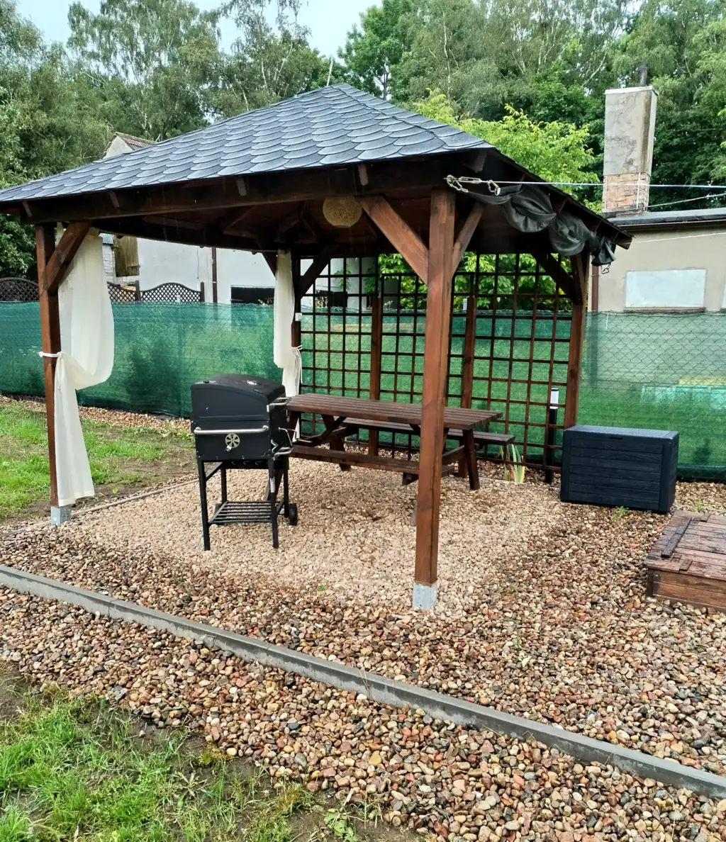 Wooden garden gazebo with a barbecue, a picnic table with benches and light curtains