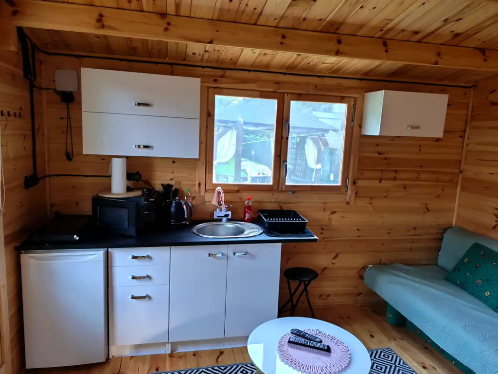 Kitchenette in cottage no. 3: white cabinets, fridge, sink, microwave and kettle, with a sofa and a round table nearby