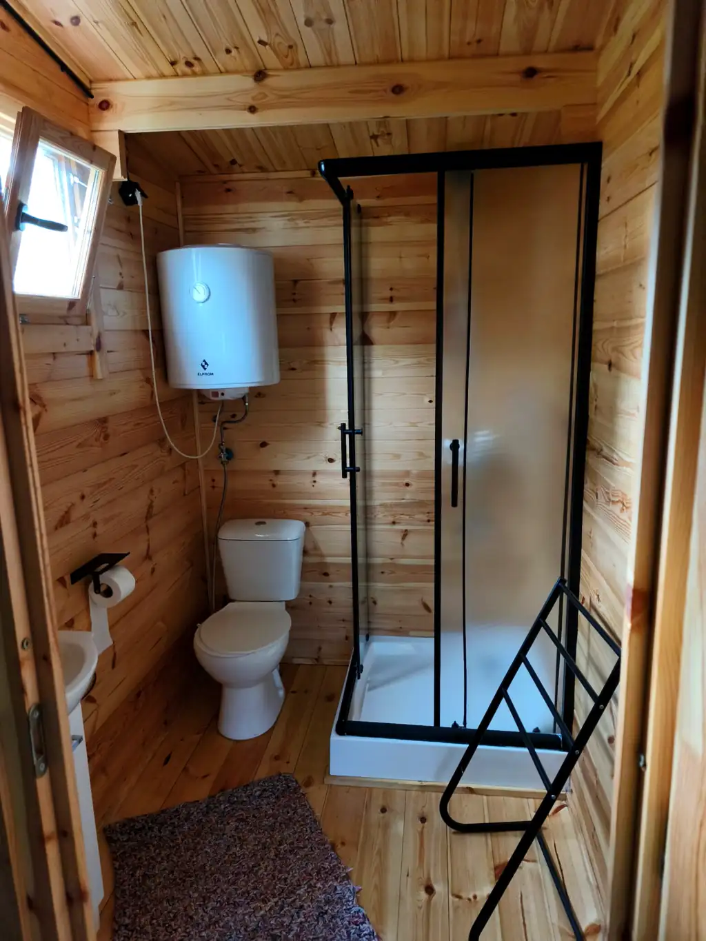 Wood-finished bathroom in cottage no. 3: shower cubicle with a black frame, toilet, washbasin and towel rail
