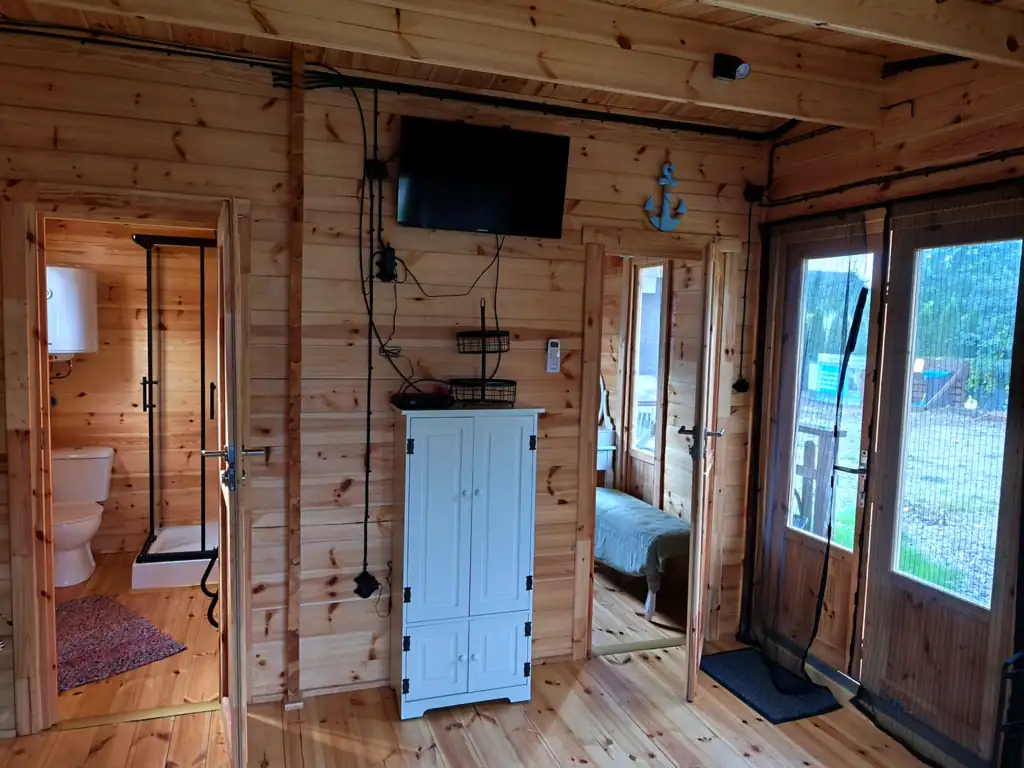 Living room in cottage no. 3: wall-mounted TV, white cabinet, doors to the bathroom and bedroom, and the terrace door