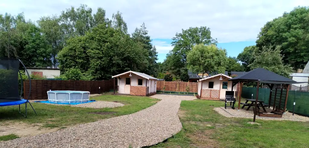 Panorama of the property in Wrzosowo: trampoline, pool, two wooden holiday cottages, gazebo, lawn and gravel path