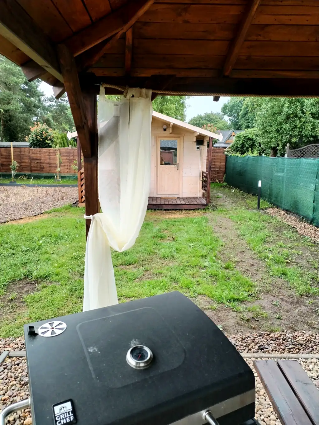 View from the gazebo across the lawn to a wooden holiday cottage, with the barbecue in the foreground